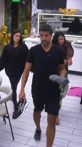 Homem com barba e duas mulheres em uma cozinha, possivelmente em um reality show.