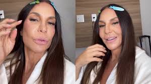 Ivete Sangalo em vídeo, com presilhas no cabelo, usando roupão branco e maquiagem.