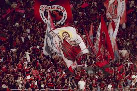 Torcida do Flamengo em estádio, com bandeiras e faixas, incluindo uma com imagem de Jesus Cristo.