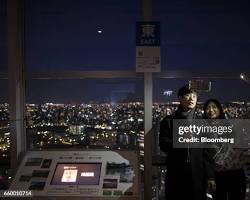 couple taking a selfie with the illuminated Fukuoka Tower in the background.の画像