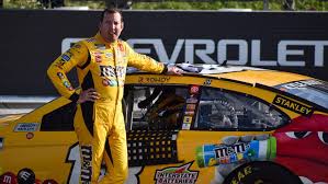 Kyle Busch poses with his No. 18 M&M's Toyota after winning the Explore the Pocono Mountains 350 Cup Series race at Pocono