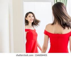 Image of woman getting dressed in front of a mirror, trying on different outfits