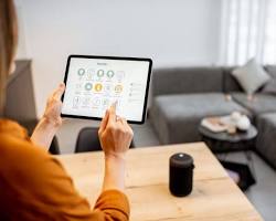 Изображение: person relaxing on a couch, using voice commands to control their smart home devices, with a futuristic cityscape in the background.