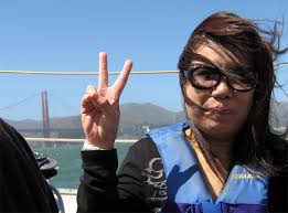 ... calmer, Evelyn flashes the peace sign. The Golden Gate bridge is behind her to the left. Evelyn smiling in front of the Golden Gate Bridge. - p06s_evelyn_wong_peace_sign_golden_gate_bridge