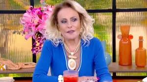 Ana Maria Braga em estúdio com flores cor-de-rosa e objetos decorativos laranjas ao fundo.