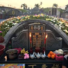 Black tombstone with gold engravings and red candles, food offerings lined un under it