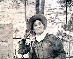 Image of Calamity Jane in her later years, posing for a photograph in a dress and hat