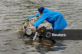 Licensable picture: A man tries to hold on to his motorbike as it falls in a flooded road during heavy rains in New Delhi