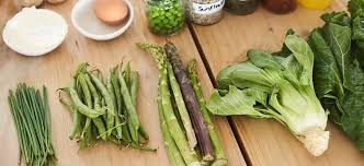 Fresh green vegetables including asparagus, green beans, bok choy, peas, and leafy greens that contain uric acid arranged on a wooden table.