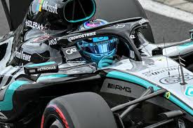 Piloto da Mercedes-AMG Petronas, George Russell, em seu carro de Fórmula 1 durante uma corrida. O capacete reflete o céu azu…