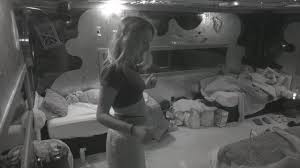 Mulher em quarto bagunçado, com cama desarrumada e roupas espalhadas. Imagem em preto e branco.