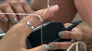 Mãos de mulher com unhas pintadas de cinza e anel no dedo, sendo examinadas por aparelho.