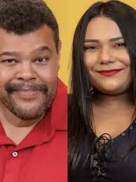 Homem sorri para a câmera com um fundo amarelo, ao lado de uma mulher com cabelo preto e batom vermelho.