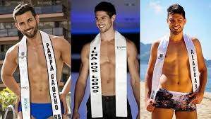 Três homens sorrindo, usando faixas de concurso de beleza com nomes de regiões do Brasil. Um deles usa sunga.