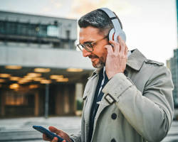 Изображение: person listening to a podcast about AI on their smartphone while commuting or exercising.
