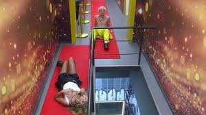 Mulher deitada em tapete vermelho e homem sentado em carrinho, em corredor decorado com luzes douradas.