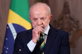 Luiz Inácio Lula da Silva, presidente do Brasil, com a mão no queixo, pensativo, com a bandeira do Brasil ao fundo.