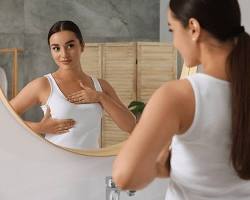 woman carefully examining her breast in front of a mirrorの画像