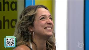 Participante do BBB 23 sorri em close-up, com o logo do programa ao fundo. Imagem de entretenimento.