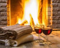 cozy winter scene with a fireplace, a warm blanket, and a glass of wine